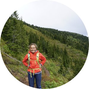 Sarah Anderson standing on a green mountain in an orange jacket