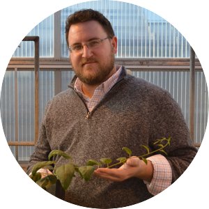 Seth Wannemuehler holding a plant with a trail of leaves in the greenhouse
