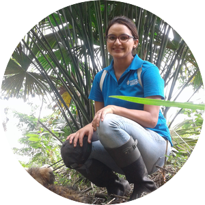 Gabriela Hidrobo wearing glasses and rain boots squatting in a rainforest 