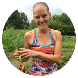 Tori Dahl standing in a farm field holding a carrot. 