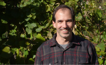man wearing a flannel standing in front of a wall of grape vines