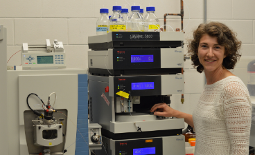 Graduate student stands in front of lab machinery 