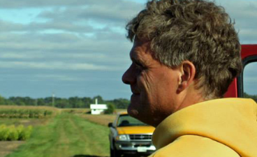 side profile of man wearing a yellow hoodie outside in a field