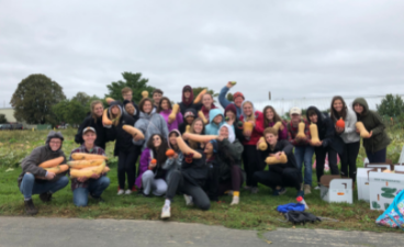 a group of college students outside holding up large squashes